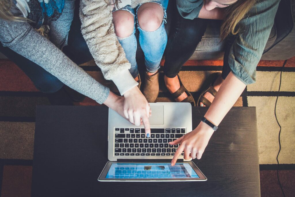 three women sitting on a sofa pointing at a laptop screen